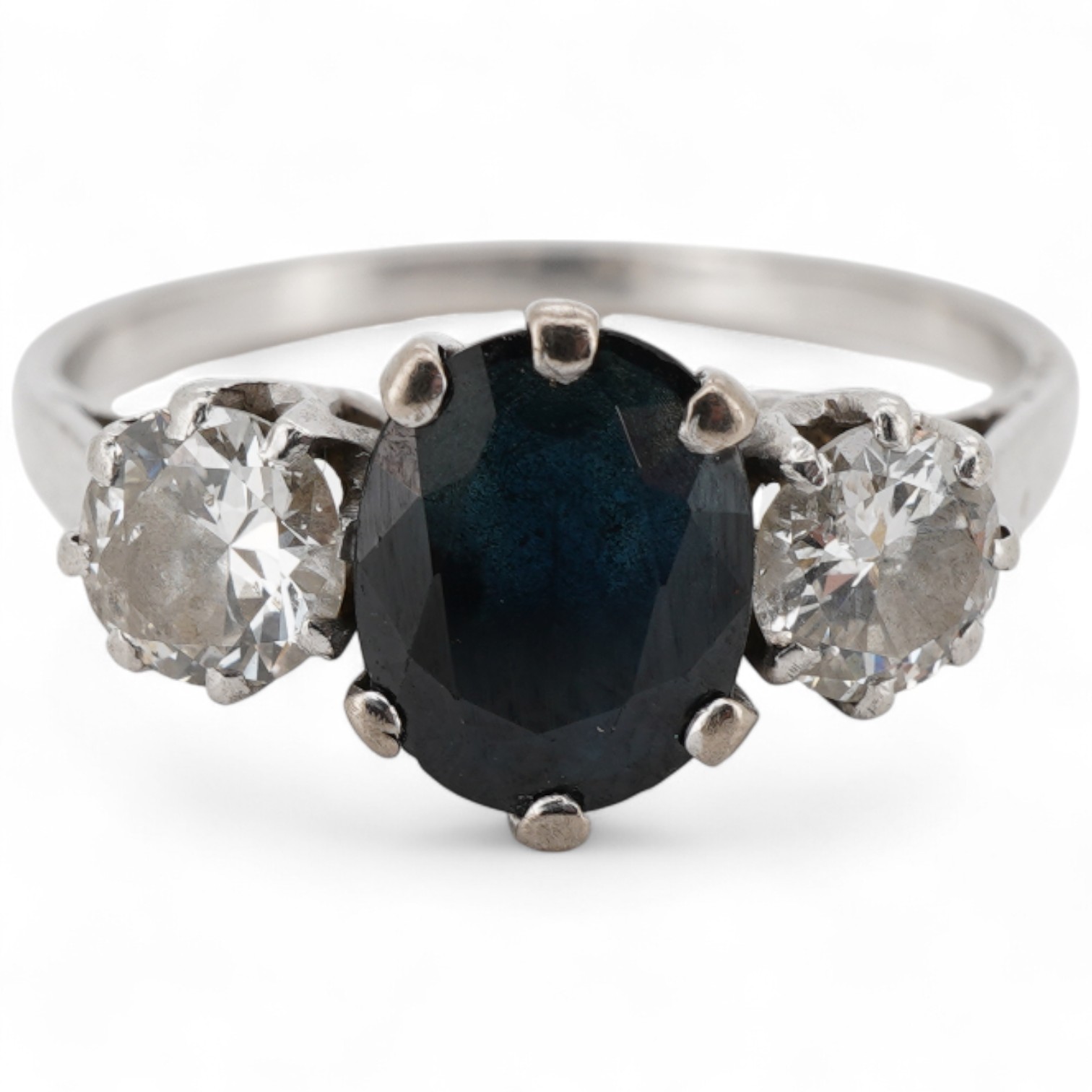 A white metal, single stone sapphire and two stone diamond set ring, the oval cut sapphire approx. 7mm by 5.8mm, the diamonds approx. 0.25ct each, size N.